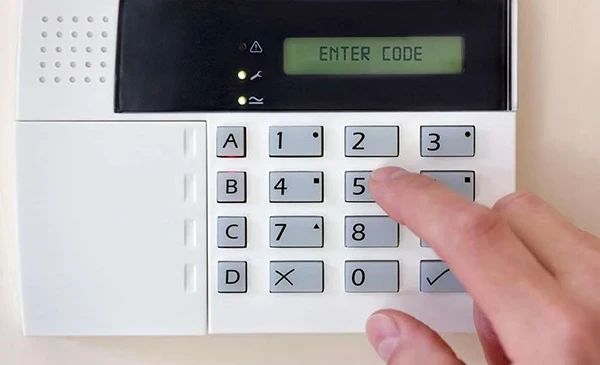 A close-up of a security alarm keypad with a person entering a security code, representing 24/7 burglar alarm services in Wellington, FL.