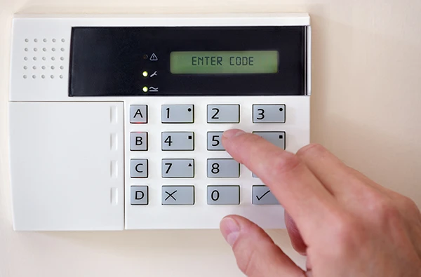 Technician arming a burglar alarm system with motion sensors and door contacts for comprehensive protection.