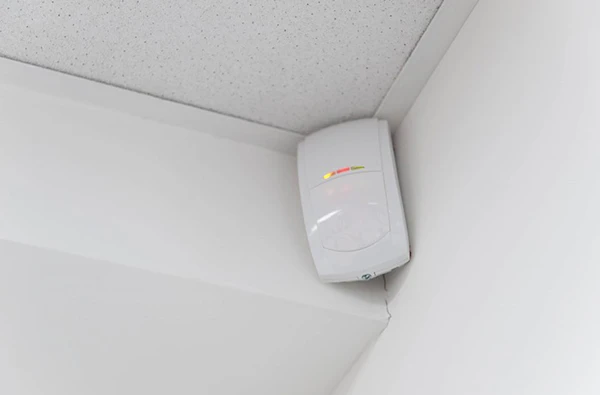 Burglar alarm sensor device installed in the corner of a room on the ceiling.