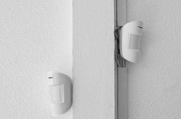 Two white motion sensors and environmental sensors installed on a white wall corner, representing advanced sensor installation services in Palm Beach Island, FL.