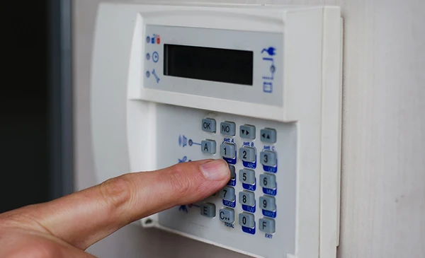 Hand pressing buttons on a burglar alarm keypad, illustrating comprehensive burglar alarm system installation services in Palm Beach Island, FL.