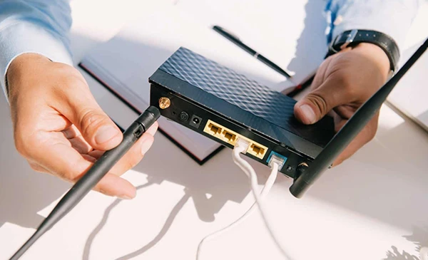 Close-up of hands adjusting antennas on a Wi-Fi internet router for better connectivity.