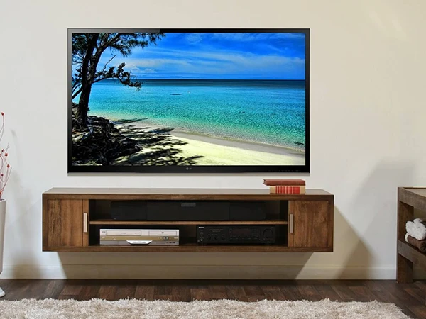 Flat-screen television mounted on a wall above a wooden media console showing a beach scene.