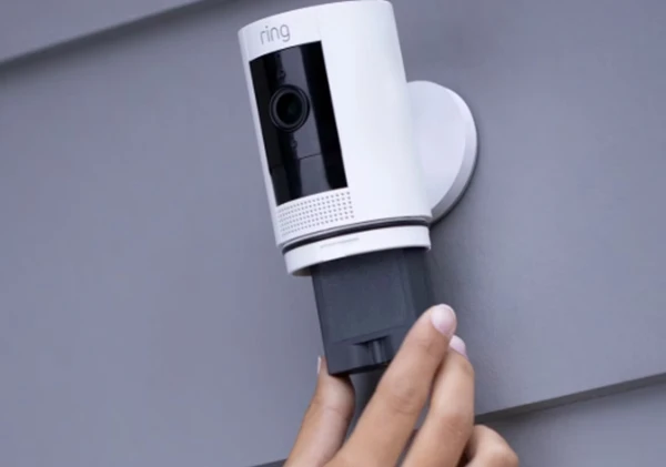 Person mounting a white Ring security camera on an exterior wall.