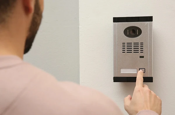 Person pressing a button on a secure intercom system installed on a wall.