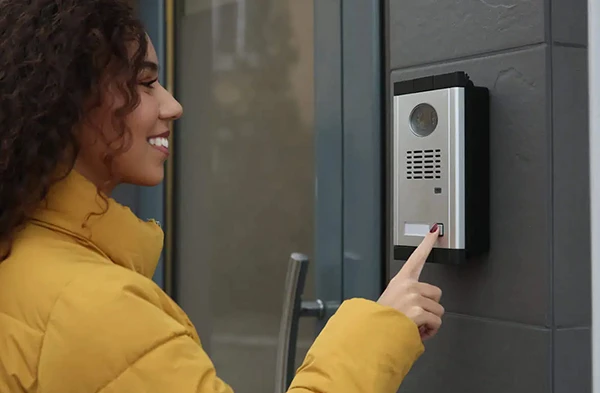 Woman pressing button on a secure intercom system mounted on an exterior wall.