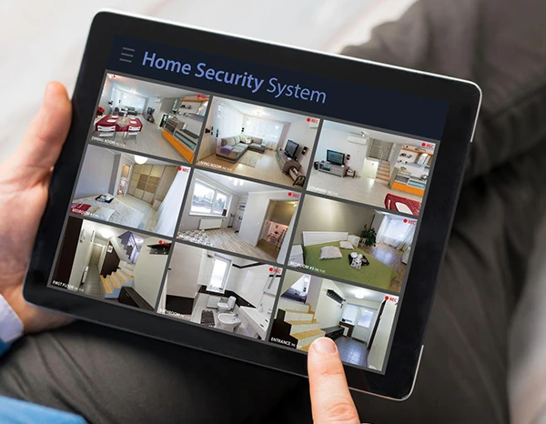 Hands holding a tablet displaying multiple surveillance camera feeds of home security system.