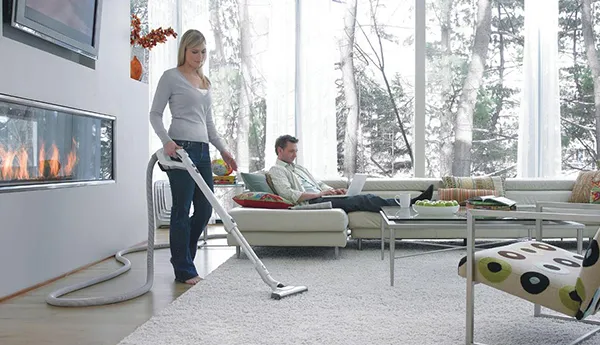 Person using central vacuum system in a modern living room with snow visible outside window.