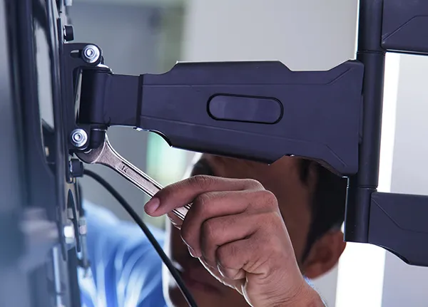 Close-up of a technician using a wrench to secure a TV mounting bracket to the wall, demonstrating professional TV mounting services.