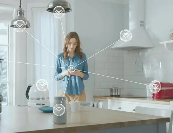 Woman interacting with voice-activated smart home device in modern kitchen, showcasing benefits of home automation installation.