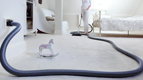 Central vacuum hose and floor cleaning setup with wall inlet in bright living space, Jupiter FL.