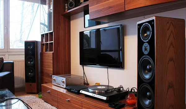 Modern living room interior with flat screen TV, tall speakers, and wooden shelves showcasing professional surround sound setup in Jupiter, FL.